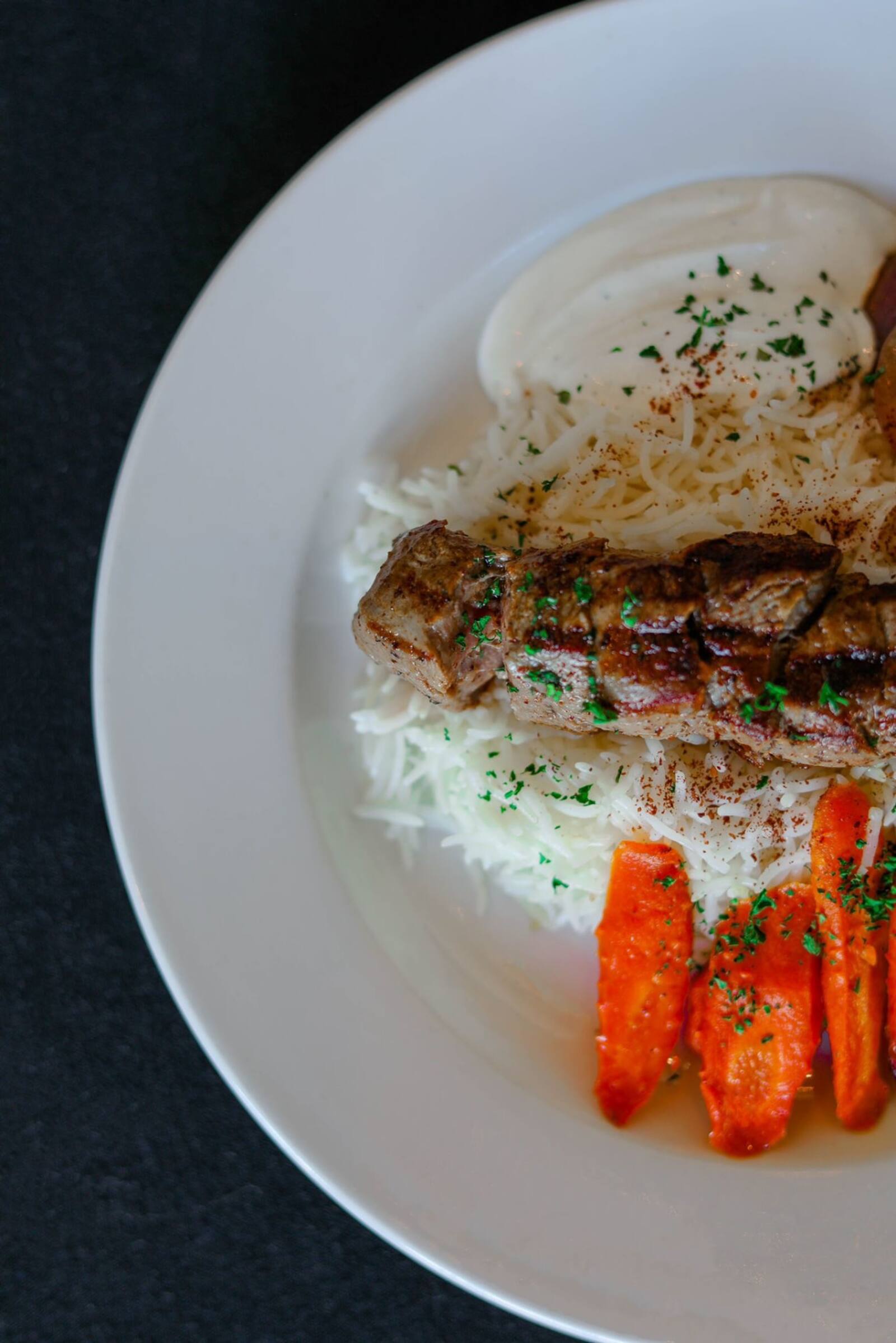 Charcoal-grilled lamb kebab over saffron basmati rice with glazed carrots and garlic yogurt