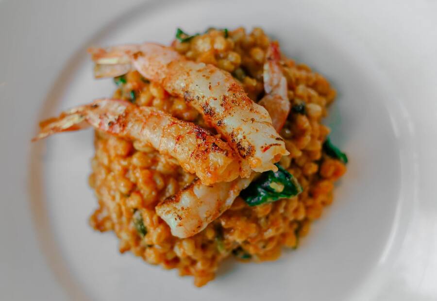 Grilled prawns resting on creamy risotto with green vegetables