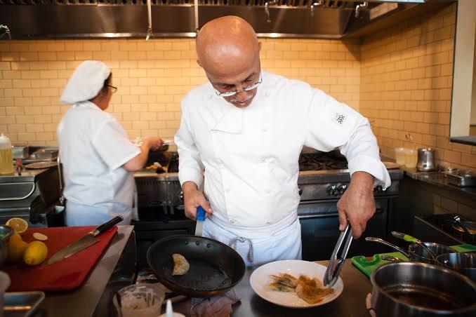 Chef-owner Saboor in a white chef coat turning food in a pan in the Angela's Eatery kitchen