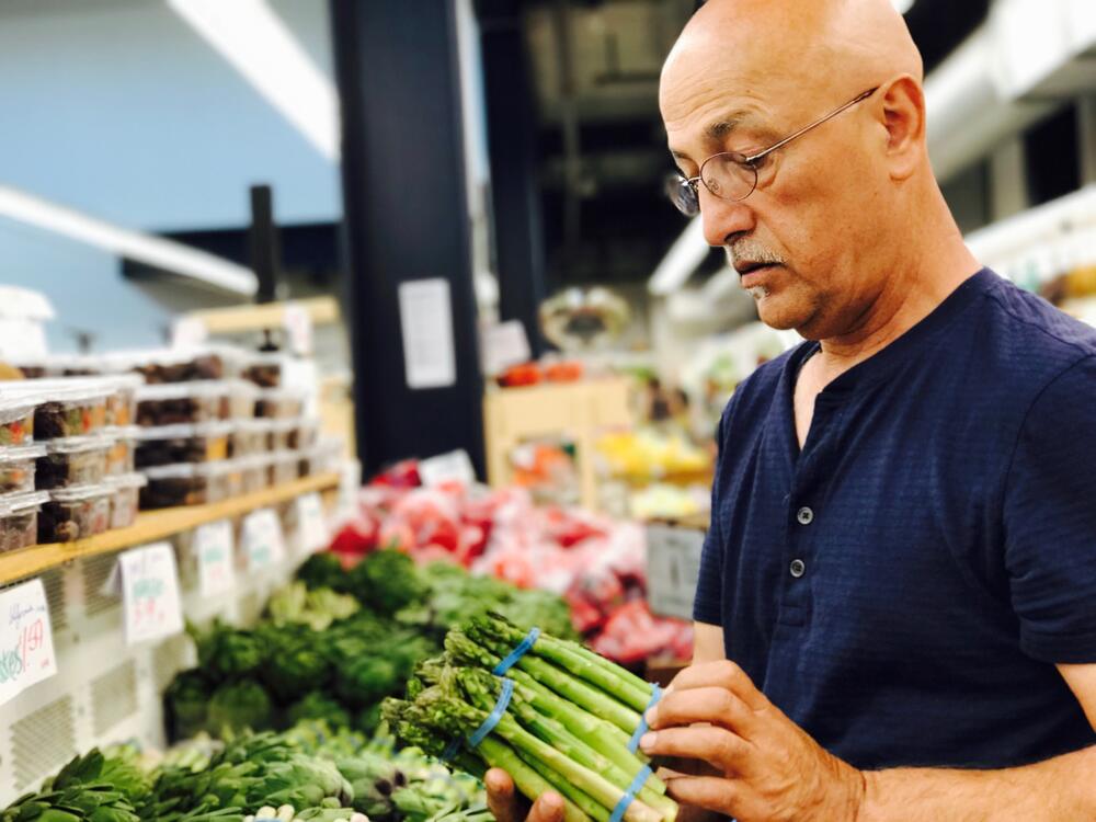 Chef Saboor inspecting a bunch of fresh green asparagus at a produce market